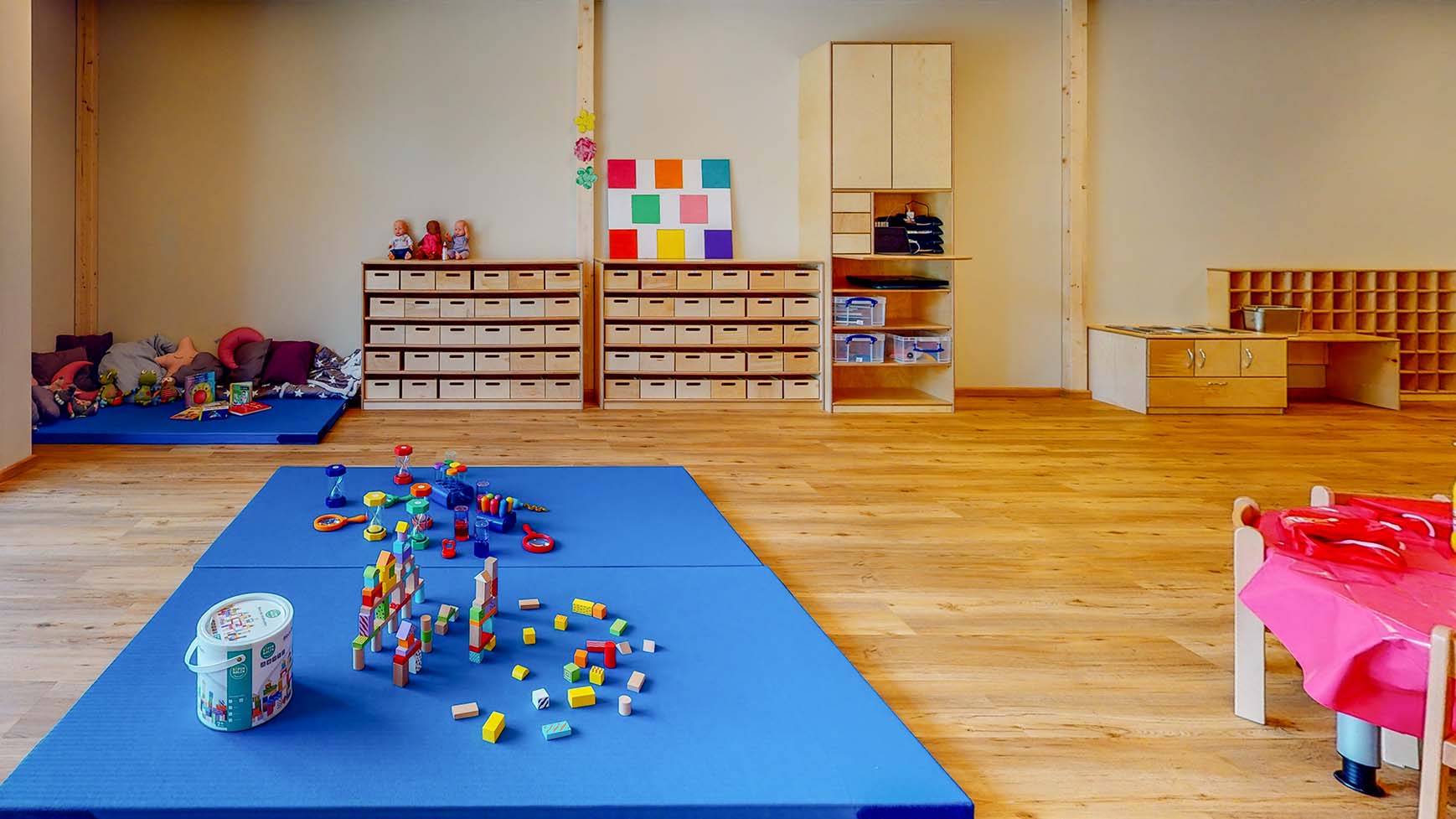 On regarde de face dans une pièce. Il y a deux matelas bleus au premier plan sur lesquels sont répartis des jouets. Grâce aux espaces de jeu communs, nos crèches favorisent les aptitudes sociales des enfants.